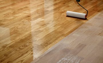 Lacquering wood floors. Worker uses a roller to coating floors. Lacquering wood floors. Worker uses a roller to coating floors. Varnishing lacquering parquet floor by paint roller - second layer. Home renovation parquet